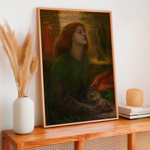 May include: A framed art print depicting a person with long red hair wearing a dark green cloak, with hands clasped together. A bright orange bird rests near the person, set against a dark, moody background with faint figures and architectural elements.
