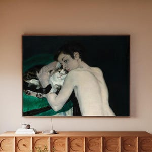 May include: A framed painting of a person cuddling a cat. The person has pale skin and dark hair, while the cat has a mix of white, brown, and black fur. The background is dark green, and the painting is in a wooden frame.