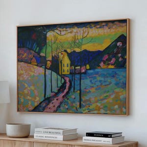 May include: Abstract landscape painting in a wooden frame. The artwork features a yellow house, a pink path, and a blue lake, with a colorful sky. The painting is displayed on a light-colored wooden cabinet.