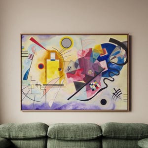 May include: Abstract painting in a wooden frame. The artwork features a vibrant mix of colors, including yellow, red, blue, and purple, with geometric shapes and lines. A black line and a black circle are also present. The painting is displayed above a green sofa.