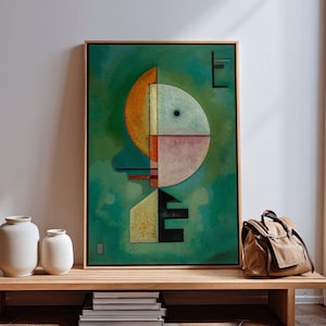 May include: Abstract art print in a wooden frame. The artwork features geometric shapes in orange, yellow, pink, and black against a green background. The framed art is displayed on a wooden bench with white vases and a brown bag.