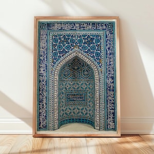 May include: Framed print featuring a detailed, ornate design in shades of blue, teal, and white. The artwork depicts an arched niche with intricate geometric patterns and calligraphy. The wooden frame adds a warm contrast to the cool tones of the print.