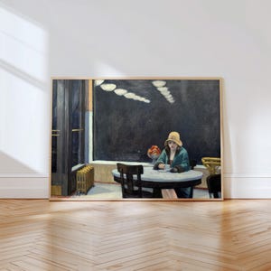 May include: A framed print of a painting depicting a person wearing a yellow hat and a teal coat sitting at a round table in a dark interior. The scene includes a bowl of fruit on the table, a radiator near a doorway, and overhead lighting fixtures.