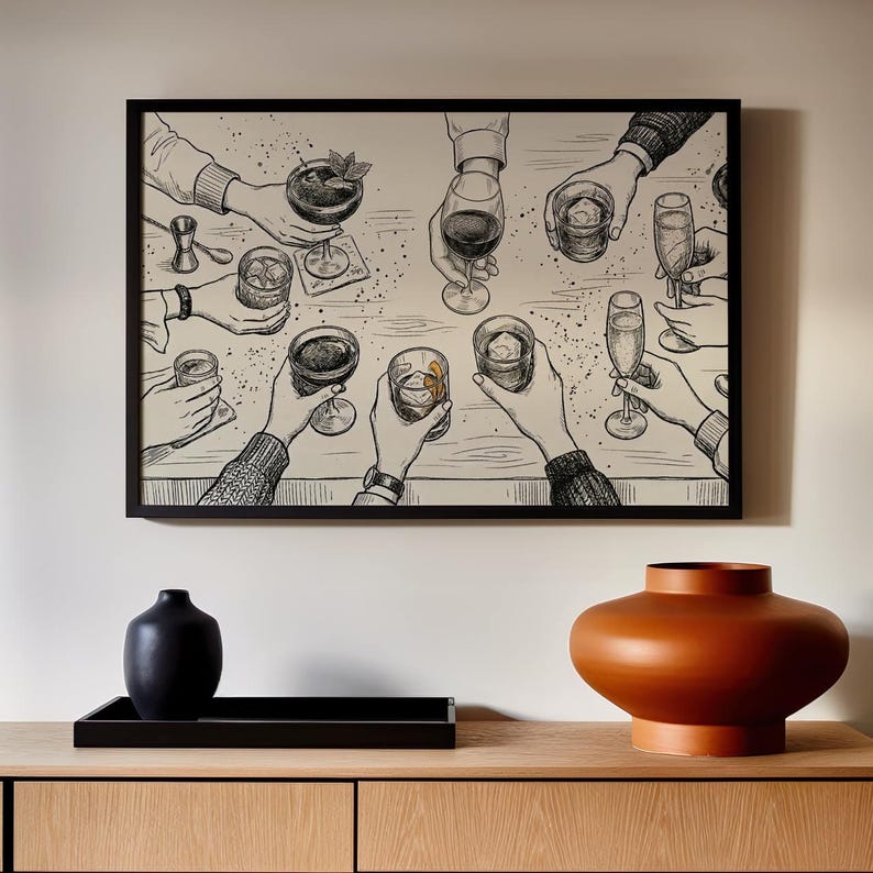 May include: Black framed art print depicting a celebratory toast with various cocktails and drinks. The black and white illustration shows hands holding glasses and cocktails, with a wooden table setting. A black vase, tray, and orange vase are in the foreground.