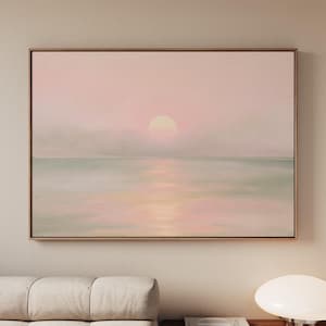 May include: A rectangular wall art print featuring a soft, hazy landscape of a calm sea under a pale pink sky. A round, glowing sun sits low on the horizon, casting a gentle, diffused reflection across the water's surface in shades of pink and green.