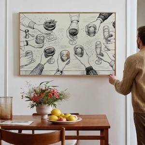 May include: A framed art print depicts a celebratory scene with hands holding various cocktails and drinks. The black and white illustration features detailed drawings of glasses, hands, and a bar setting, perfect for a home bar or dining area.