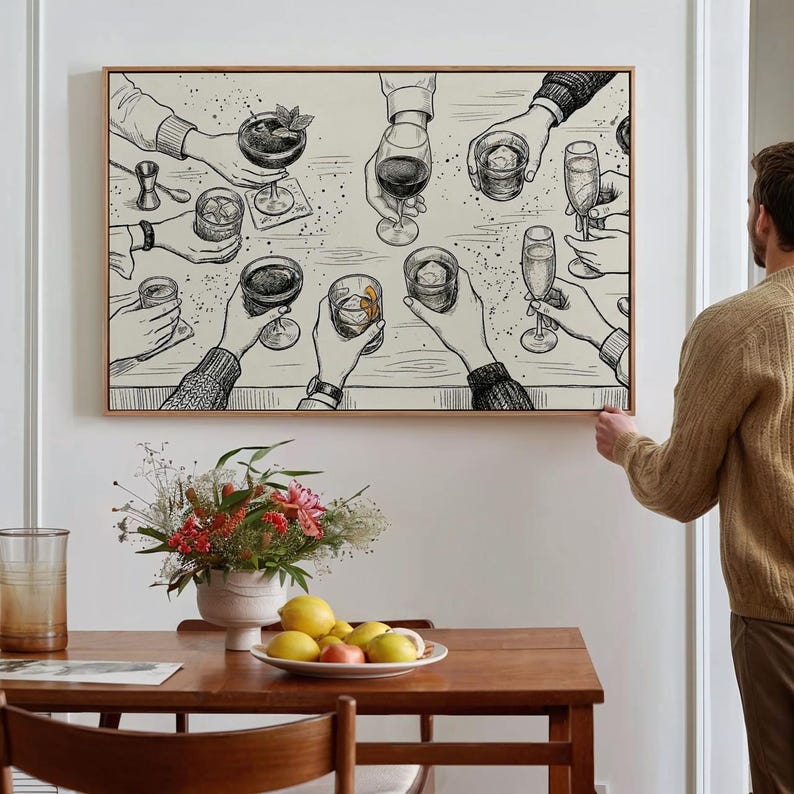 May include: A framed art print depicts a celebratory scene with hands holding various cocktails and drinks. The black and white illustration features detailed drawings of glasses, hands, and a bar setting, perfect for a home bar or dining area.