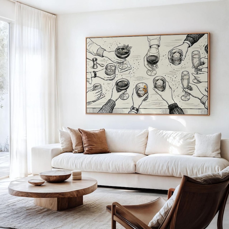 May include: A framed art print depicts a celebratory toast with various cocktails and drinks. The black and white illustration shows multiple hands holding glasses, creating a lively and social scene. The artwork is displayed above a white sofa.