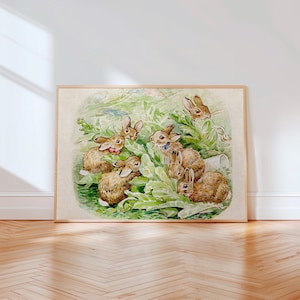 May include: A framed watercolor print featuring a group of brown rabbits nestled among green leafy plants. The rabbits are depicted in various poses, some wearing small colored collars, set against a soft, light-colored background within a wooden frame.