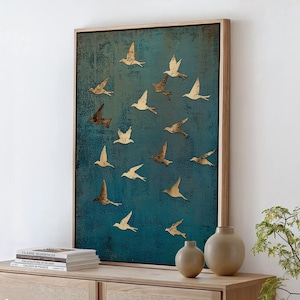 May include: A framed artwork featuring a flock of birds in flight against a textured teal background. The birds are in various shades of brown and cream. The artwork is displayed above a wooden cabinet with two beige vases and books.