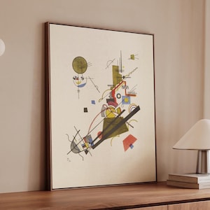 May include: Abstract art print in a wooden frame. The artwork features geometric shapes and lines in red, yellow, black, and blue on a cream background. The composition includes circles, squares, and diagonal lines, creating a dynamic visual.