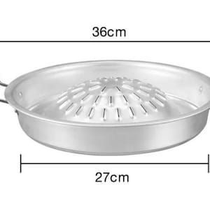 Puede incluir: Sartén redonda de plata para asar con asas negras y un inserto de parrilla elevado. La sartén mide 27 cm de diámetro y 9 cm de altura.