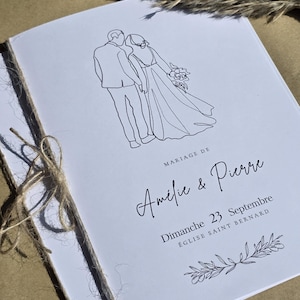 Peut inclure: Un programme de mariage blanc, lié avec de la ficelle. La couverture présente un dessin au trait d'un couple et le texte "Mariage de Amélie & Pierre, Dimanche 23 Septembre, Église Saint Bernard."