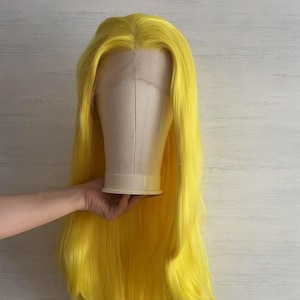 May include: A bright yellow wig with long, straight hair. The wig is on a mannequin head.
