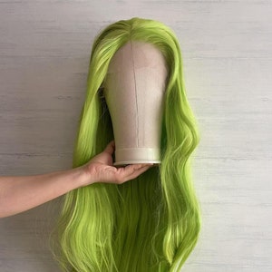 Puede incluir: Una peluca larga de color verde brillante con un estilo recto y fluido. La peluca se muestra en una cabeza de maniquí blanca.