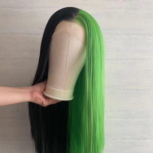 May include: A long, straight wig with half black and half bright green hair. The wig is on a mannequin head.