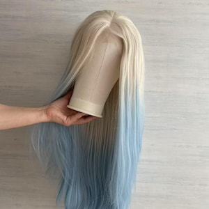 Könnte beinhalten: Lange, blonde Perücke mit hellblauem Ombre-Effekt. Die Perücke ist mit langen, geraden Strähnen versehen und wird auf einem Schaufensterkopf präsentiert. Das Haar wechselt von blond zu blau und erzeugt einen auffälligen Kontrast.