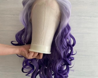 Puede incluir: Una peluca larga y rizada con un degradado de color de morado claro a morado oscuro. La peluca está en una cabeza de maniquí.
