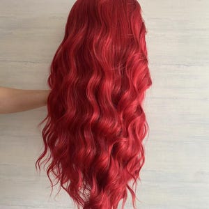 Puede incluir: Una peluca larga y ondulada de color rojo brillante. La peluca est&aacute; peinada en ondas sueltas y tiene un acabado de aspecto natural.