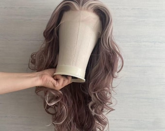 May include: A long, wavy wig with a blend of mauve and light blonde tones. The wig is styled with loose curls and is mounted on a canvas wig stand. The hair has a natural-looking hairline.