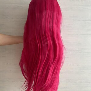 Pode incluir: Uma peruca longa e ondulada em um tom vibrante de f&uacute;csia. A peruca tem uma linha de cabelo de apar&ecirc;ncia natural e &eacute; estilizada com ondas soltas. O cabelo cai, criando uma apar&ecirc;ncia cheia e volumosa. A peruca &eacute; provavelmente feita de fibras sint&eacute;ticas.