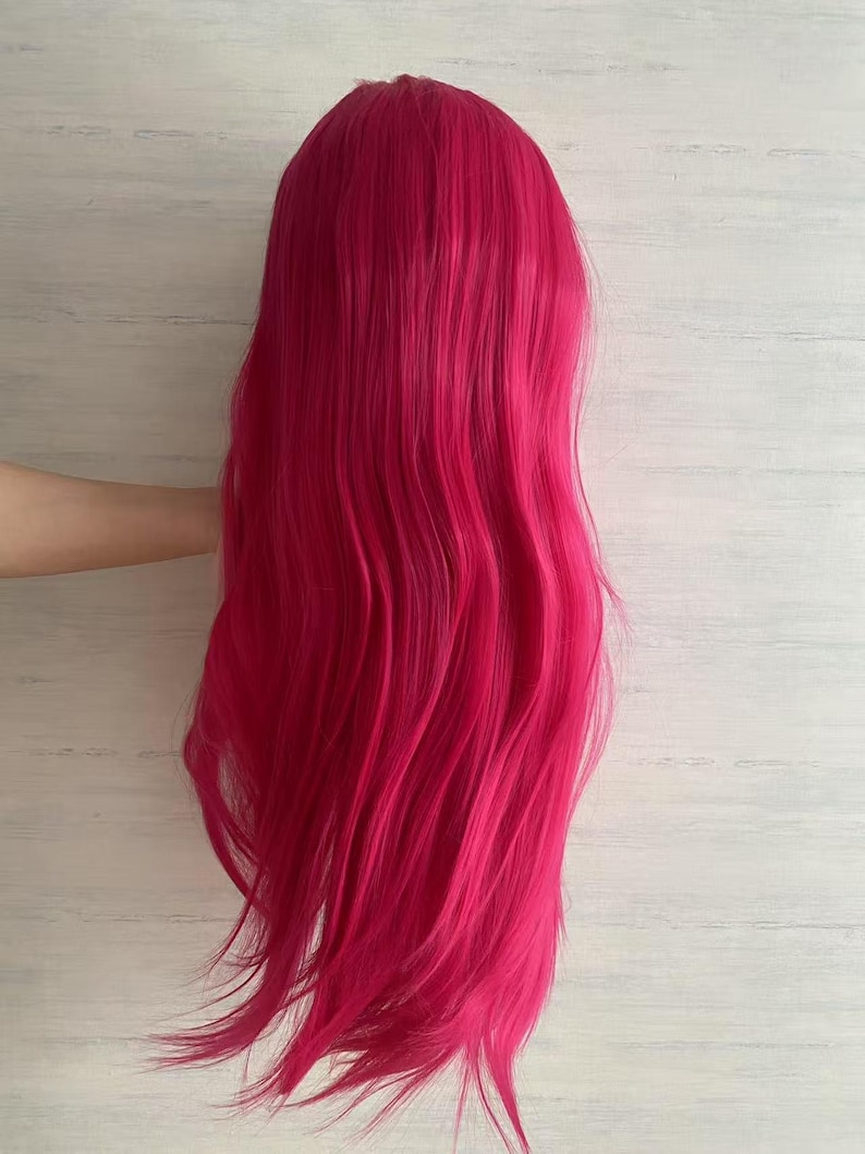 Pode incluir: Uma peruca longa e ondulada em um tom vibrante de f&uacute;csia. A peruca tem uma linha de cabelo de apar&ecirc;ncia natural e &eacute; estilizada com ondas soltas. O cabelo cai, criando uma apar&ecirc;ncia cheia e volumosa. A peruca &eacute; provavelmente feita de fibras sint&eacute;ticas.