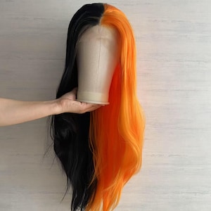 May include: A two-tone wig, split vertically with black on one side and bright orange on the other. The long, wavy hair is displayed on a mannequin head. The wig is likely synthetic, with a natural-looking hairline.
