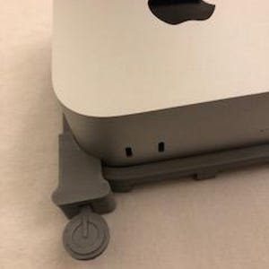 May include: A white and grey Apple Mac Mini computer with the Apple logo. The computer is connected to a grey power adapter. The power button is visible on the adapter.