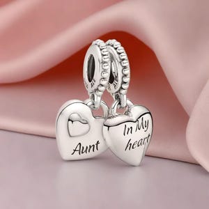以下が含まれることがあります： 銀製のチャームに、ハート型のペンダントが2つ付いています。1つのハートには「叔母」と書いてあり、もう1つのハートには「私の心の中に」と書いてあります。