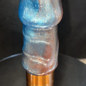 May include: A decorative object with a metallic finish. The top portion is a blend of blue and copper hues, with a glittery effect. The base is a copper-colored cylinder. The object is standing upright.