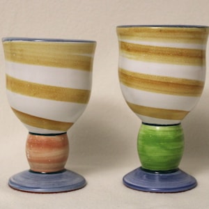 Puede incluir: Dos vasos para beber de cerámica con diseños a rayas. El vaso de la izquierda tiene un diseño a rayas blancas y marrones con una base naranja claro y azul. El vaso de la derecha tiene un diseño a rayas blancas y marrones con una base verde y azul.