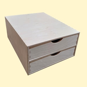 May include: A two-drawer wooden storage box with a natural wood finish. The drawers are made of plywood and have a simple design.