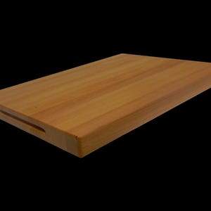 May include: A large, rectangular wooden chopping board with a natural wood finish. The board has a handle cut out on one side.