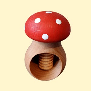May include: A wooden nutcracker shaped like a red and white mushroom. The mushroom has white polka dots on the top and a wooden screw in the bottom.