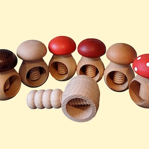 May include: A set of wooden nutcrackers shaped like mushrooms. The nutcrackers are in various colours, including red, brown, and natural wood. Some of the mushrooms have white polka dots.