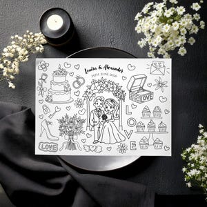 Op de afbeelding: Zwart-wit huwelijk illustratie met bruid en bruidegom, taart, ringen en cupcakes. De tekst "Louisa & Alexander 25th June 2026" is zichtbaar. De afbeelding ligt op een bord, met kaars en bloemen.