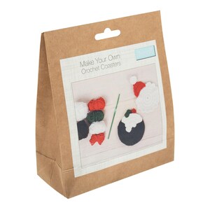 May include: A brown paper bag containing a crochet coaster kit. The kit includes yarn in red, white, green, and black, a crochet hook, and instructions. The image on the package shows a Santa hat and a Christmas pudding coaster design. The text on the package reads "Make Your Own Crochet Coasters."