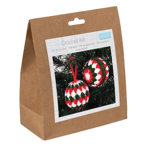 May include: A brown paper bag labeled "Crochet Kit" with two crocheted Christmas ornaments. The ornaments are red, white, and green, with a red hanging string. The ornaments are displayed on a green Christmas tree.