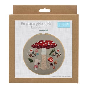 May include: An embroidery hoop kit with a toadstool design. The kit includes a wooden hoop with a beige fabric, embroidered with a red and white mushroom, smaller mushrooms, and floral accents. The packaging is a brown cardboard box. Finished hoop size: 15cm x 15cm / 6".