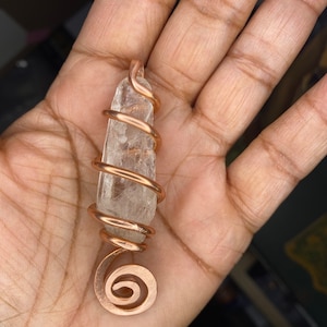 May include: A clear quartz crystal wrapped in a copper wire spiral. The wire is a rose gold color and is wrapped around the crystal in a tight spiral. The crystal is about 2 inches long and the wire is about 1/4 inch thick.