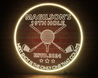 Puede incluir: Un letrero de neón blanco con una bola de golf y palos de golf cruzados. El letrero dice "Magilson's 19th Hole Estd. 2024 Next shot is the only one that counts".