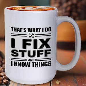 May include: White ceramic coffee mug with black text that reads "That's what I do I fix stuff and I know things". The text is surrounded by two black lines. There is a wrench and screwdriver symbol between the words "I" and "fix".