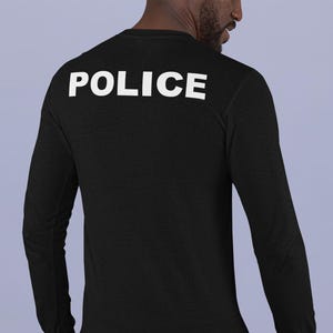 以下が含まれることがあります： 背中に白で「POLICE」とプリントされた黒の長袖シャツ。 シャツは柔らかく暗い生地でできており、クルーネックです。