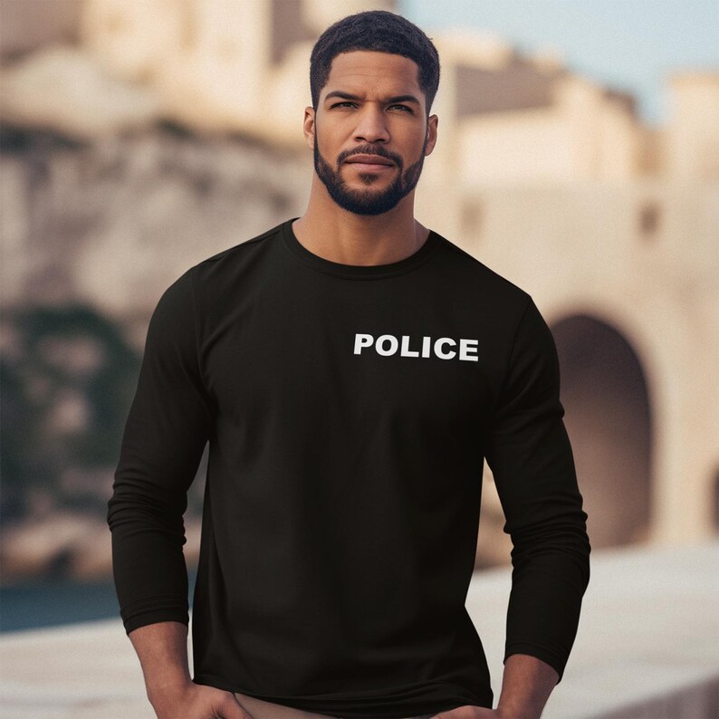 以下が含まれることがあります： 胸に白で「POLICE」とプリントされた黒の長袖シャツ。シャツは柔らかく不透明な素材で作られています。シャツはクルーネックです。