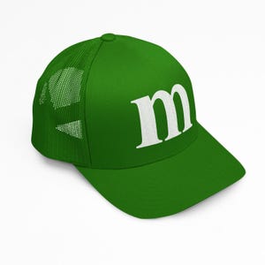 Puede incluir: Gorra de camionero verde con una 'm' blanca bordada en el panel frontal. La gorra tiene una parte trasera de malla para mayor transpirabilidad y una visera curva. La gorra es de color verde liso.