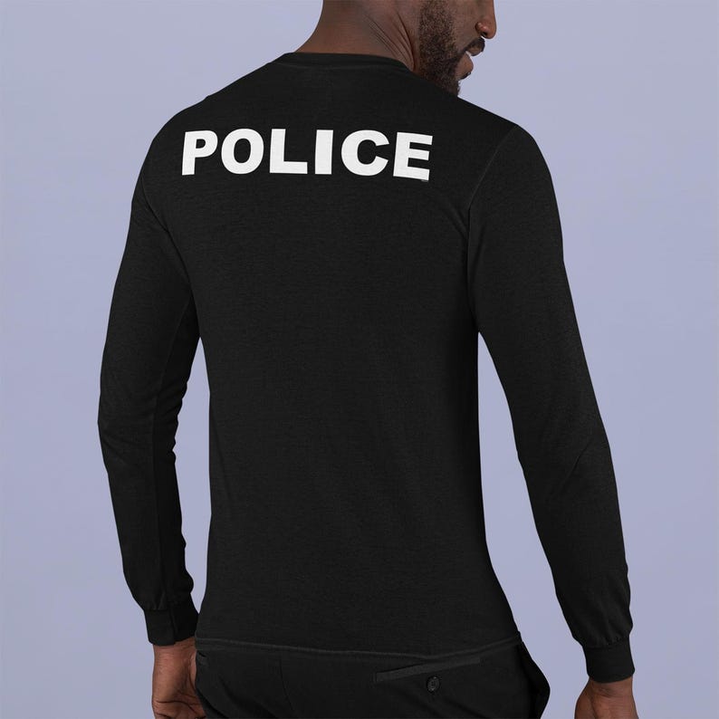 以下が含まれることがあります： 背中に白で「POLICE」とプリントされた黒の長袖シャツ。 シャツは柔らかく暗い生地でできており、クルーネックです。