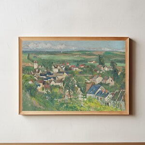 Peut inclure: Une peinture de paysage encadrée représentant un village niché dans une vallée avec des collines verdoyantes, des arbres et des maisons aux toits bleus et rouges sous un ciel nuageux. L'œuvre est insérée dans un cadre en bois clair rectangulaire.