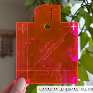 Peut inclure: Un guide de couture en plastique orange vif avec des marques en pouces et en fractions de pouce. Le guide a une grille et comprend le texte "kimtsu seam guide kimtsu nit zin: comes in handy".