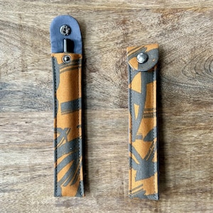 May include: Two fabric pen cases with a brown and black geometric pattern. The cases have a blue flap with a button closure.