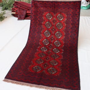 May include: A rectangular area rug featuring a deep red and black color palette. The central field displays a repeating pattern of geometric octagonal motifs in white, black, and red, framed by a wide, dark border with intricate linear detailing.